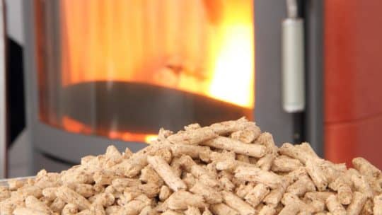Tas de granulés bois en premier plan devant une chaudière à pellets en fonctionnement
